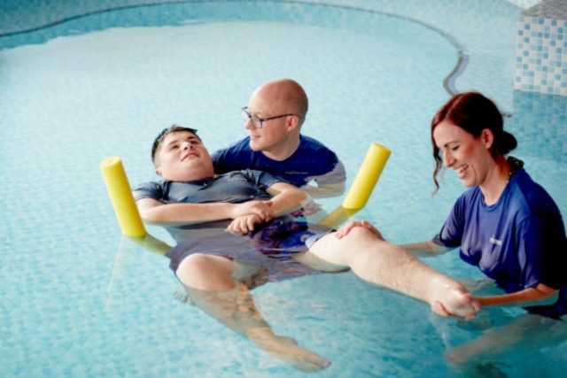 A young person with two physiotherapists in the Rainbows pool