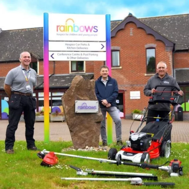Three men standing outside Rainbows with gardening equipment