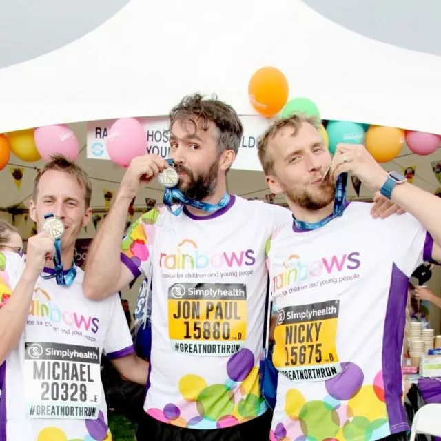 Three runners kissing their Great North Run medals