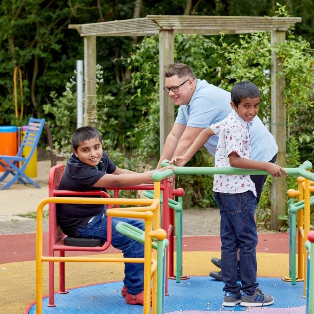 A family outside playing on a roundabout